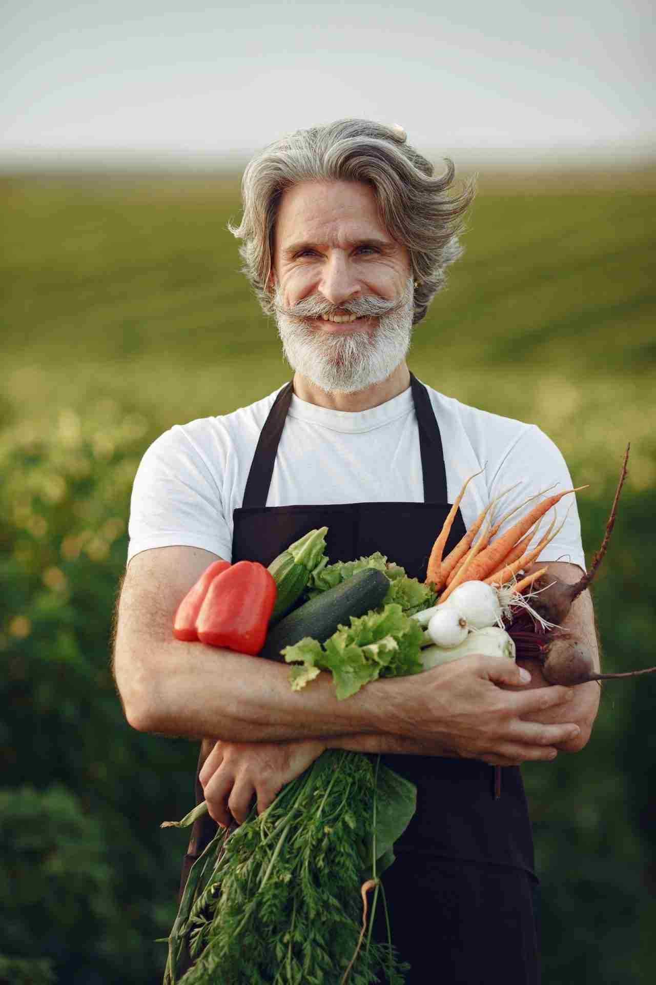 Produttore siciliano sorridente con verdure fresche in braccio